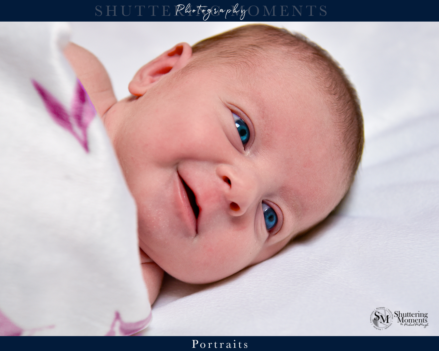 Newborn baby with bright blue eyes and a big smile, wrapped in a cozy blanket.