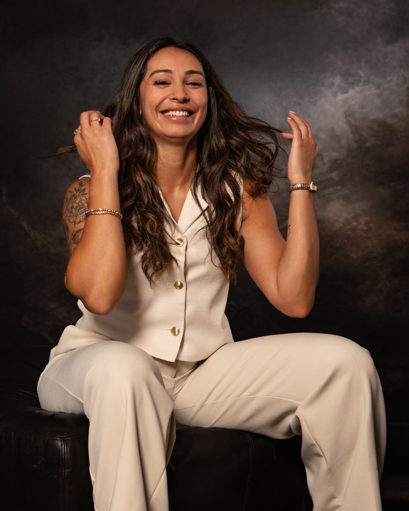 Ana Sanchez seated against a black backdrop, brushing her hair to the side during a professional real estate branding portrait session.
