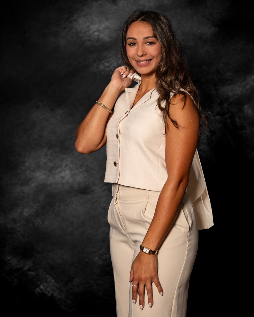 Ana Sanchez standing in a cream-colored outfit against a black studio backdrop for a professional realtor portrait.