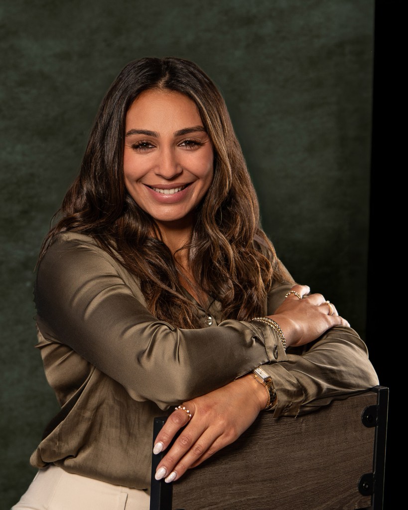 Ana Sanchez posing confidently behind a studio chair in an olive green silk shirt and cream pants for professional realtor branding photography.