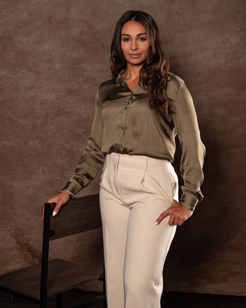 Ana Sanchez standing beside a studio chair in an olive green silk shirt and cream pants during a professional real estate branding session.