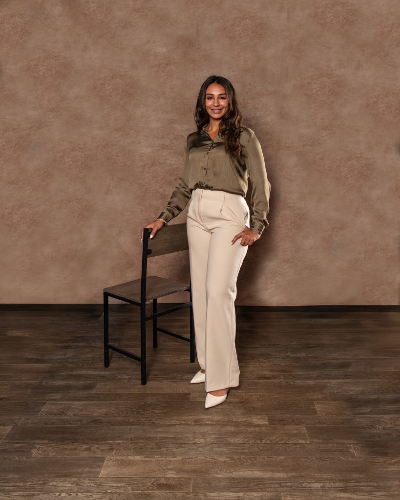 Ana Sanchez standing beside a studio chair wearing an olive green silk shirt and cream pants during a professional real estate branding session.